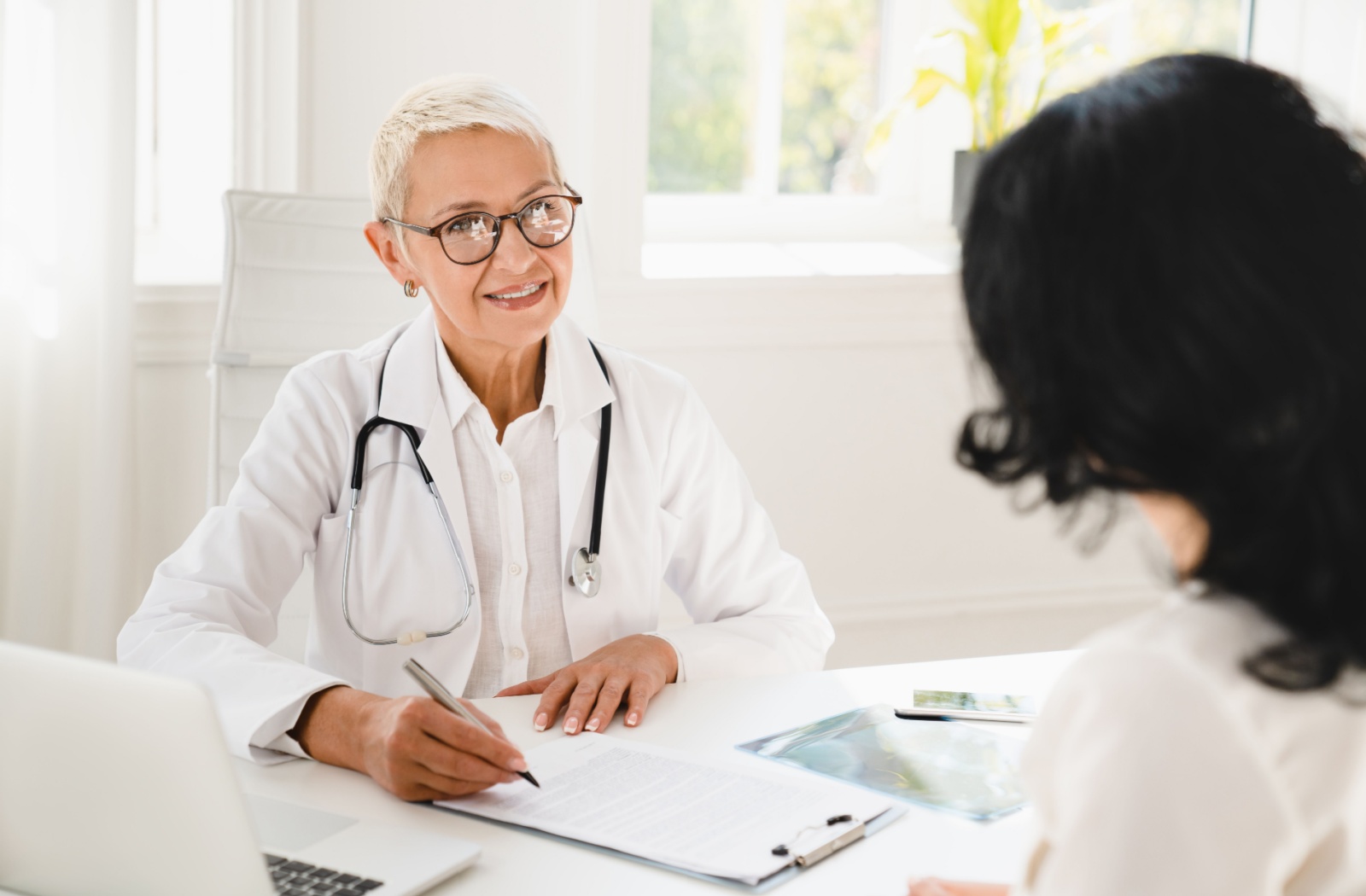An orofacial myofunctional therapist discusses myofunctional therapy with a patient in a bright medical office.